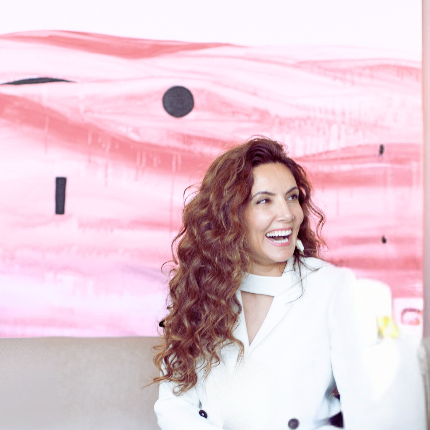 Rita Rawashdeh with curly hair smiling in front of a pink and white abstract painting
