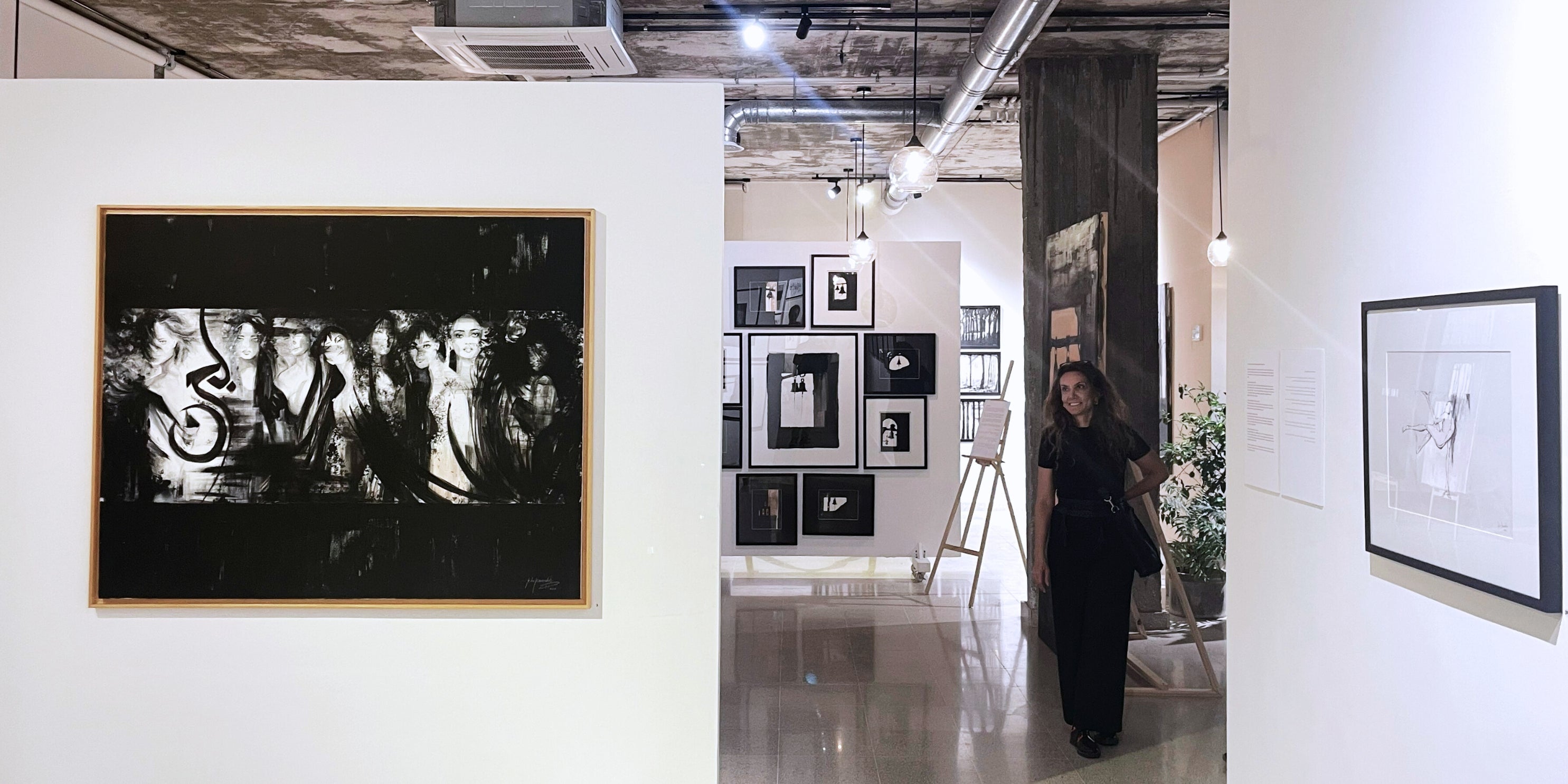 Art gallery with framed artworks on white walls, with Rita Rawashdeh observing the display.
