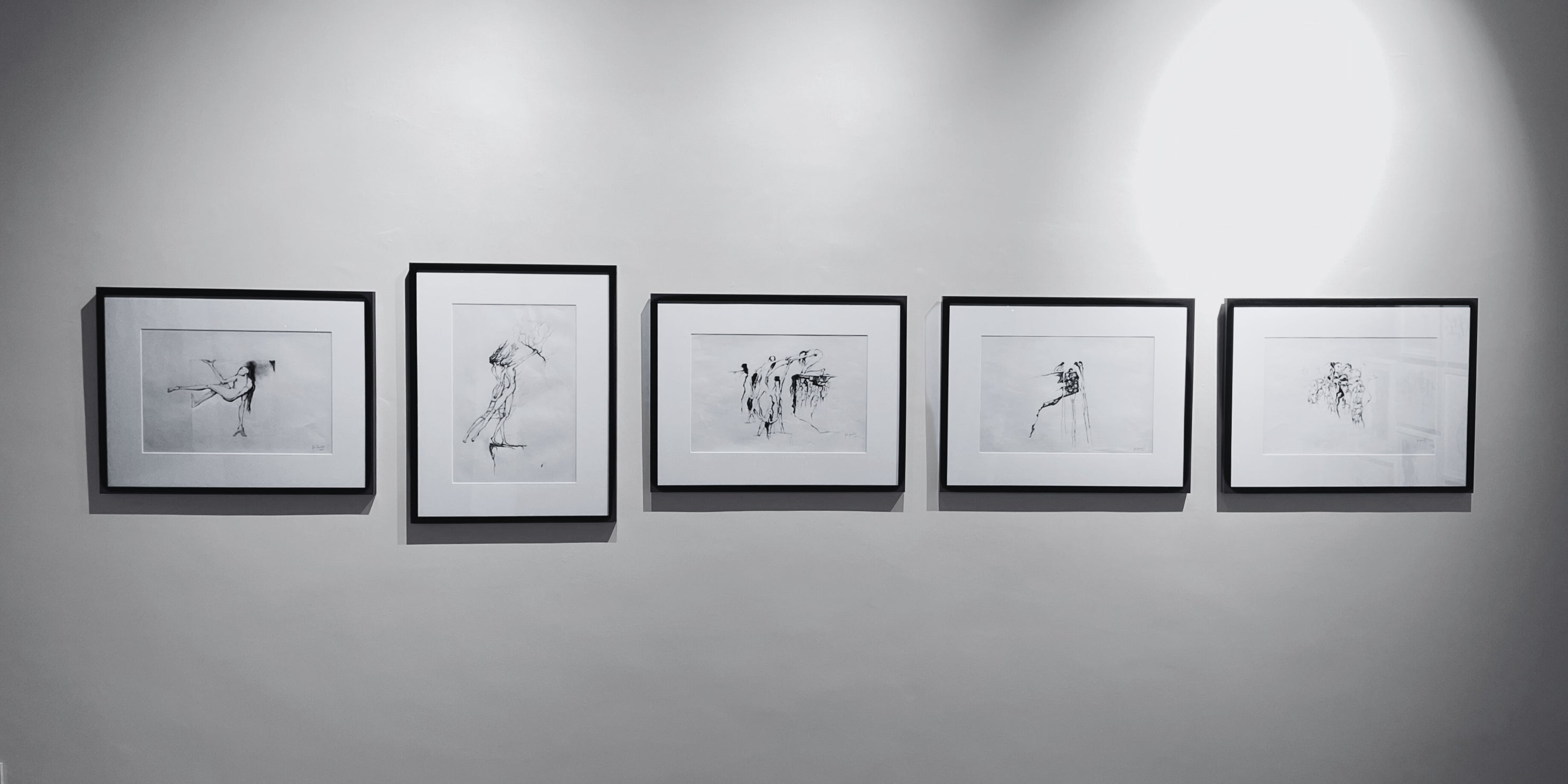 Five framed black and white artworks on a gray wall by Rita Rawashdeh