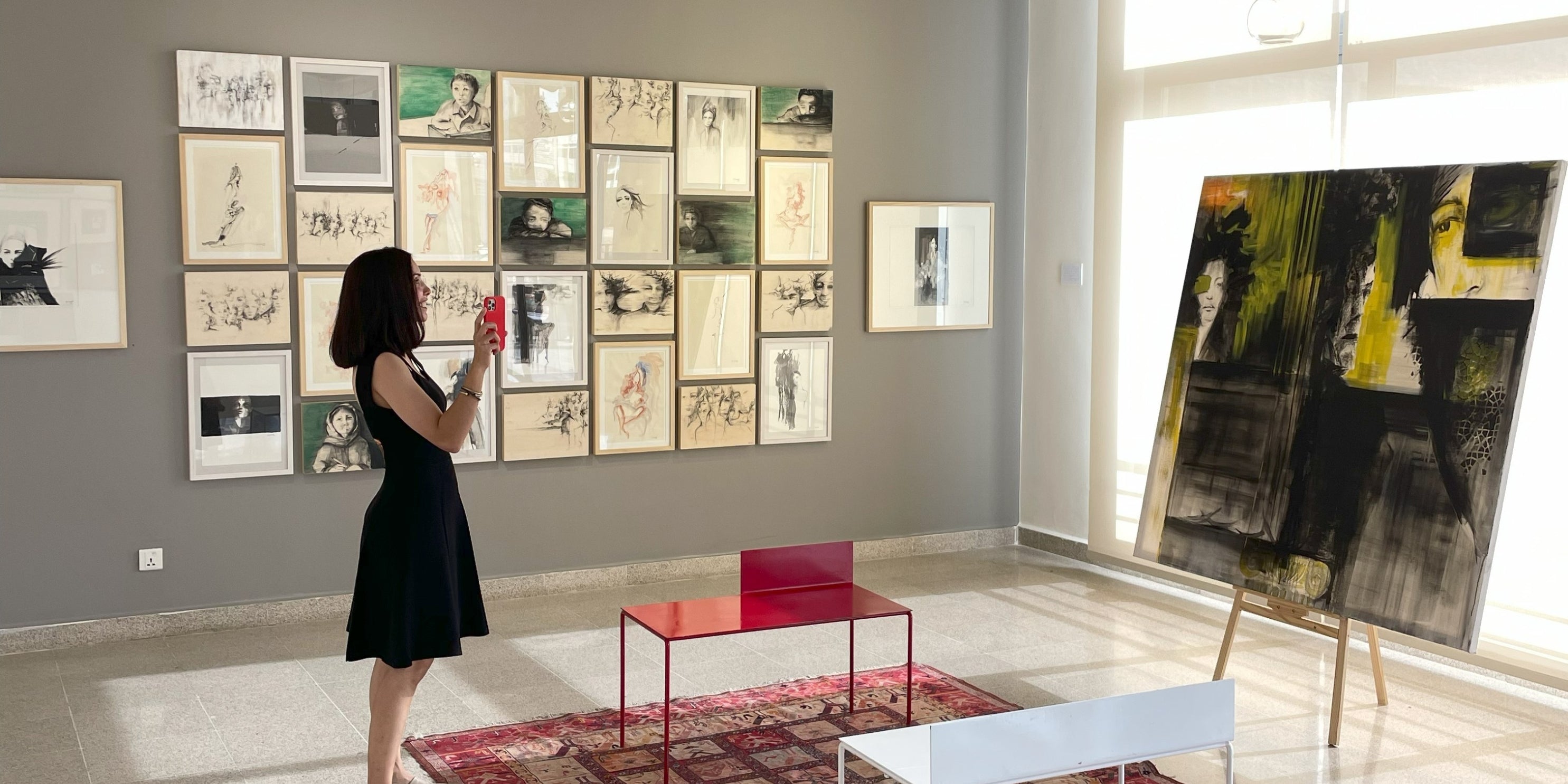 Rita Rawashdehin a black dress standing in an art gallery with various artworks on the walls. 